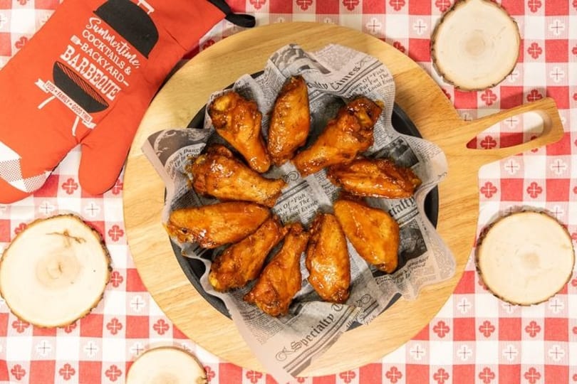 Glazed chicken wings in a skillet lined with newspaper, on a red and white checkered tablecloth.